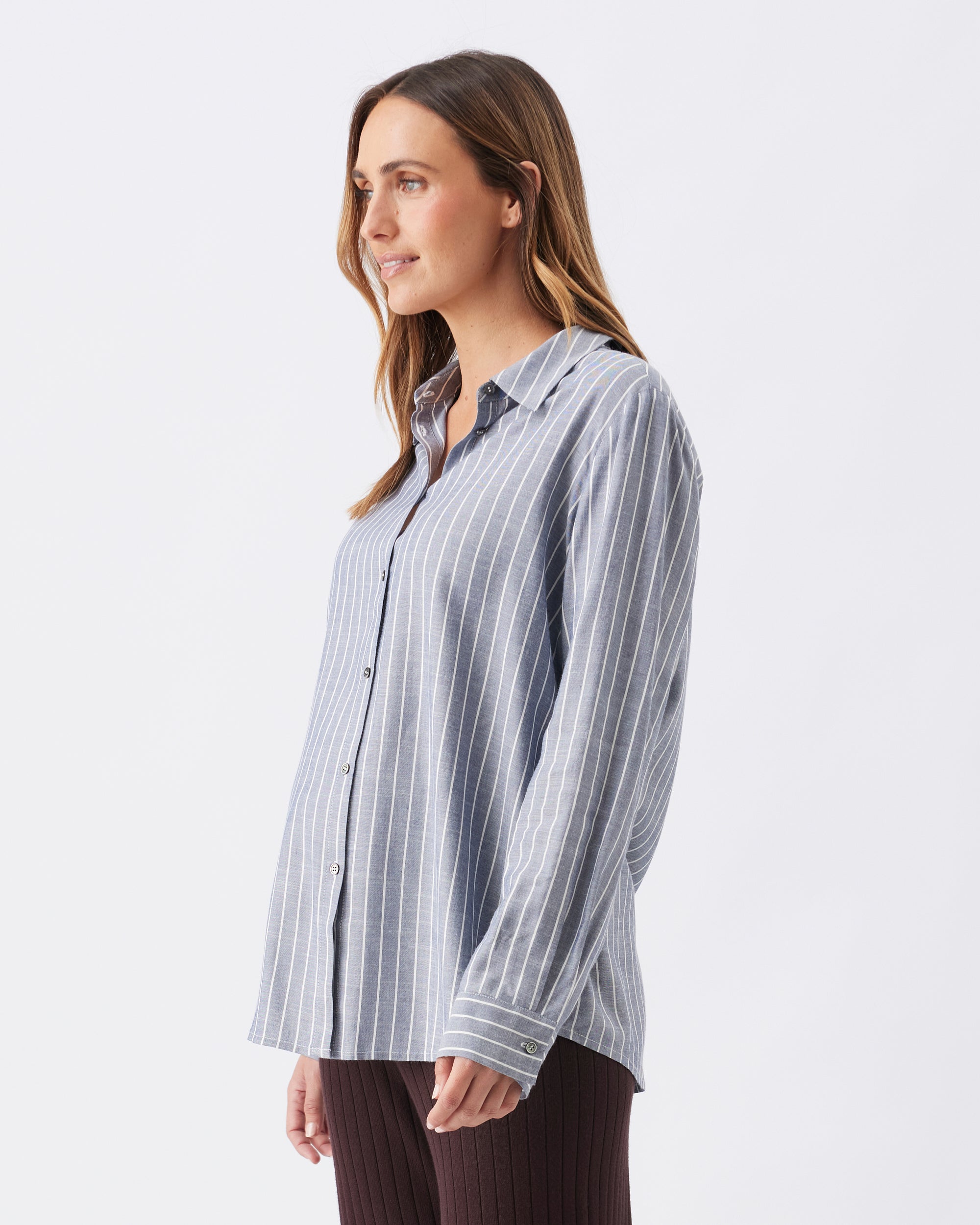 Side view of a pregnant woman wearing a light blue striped shirt on a white background