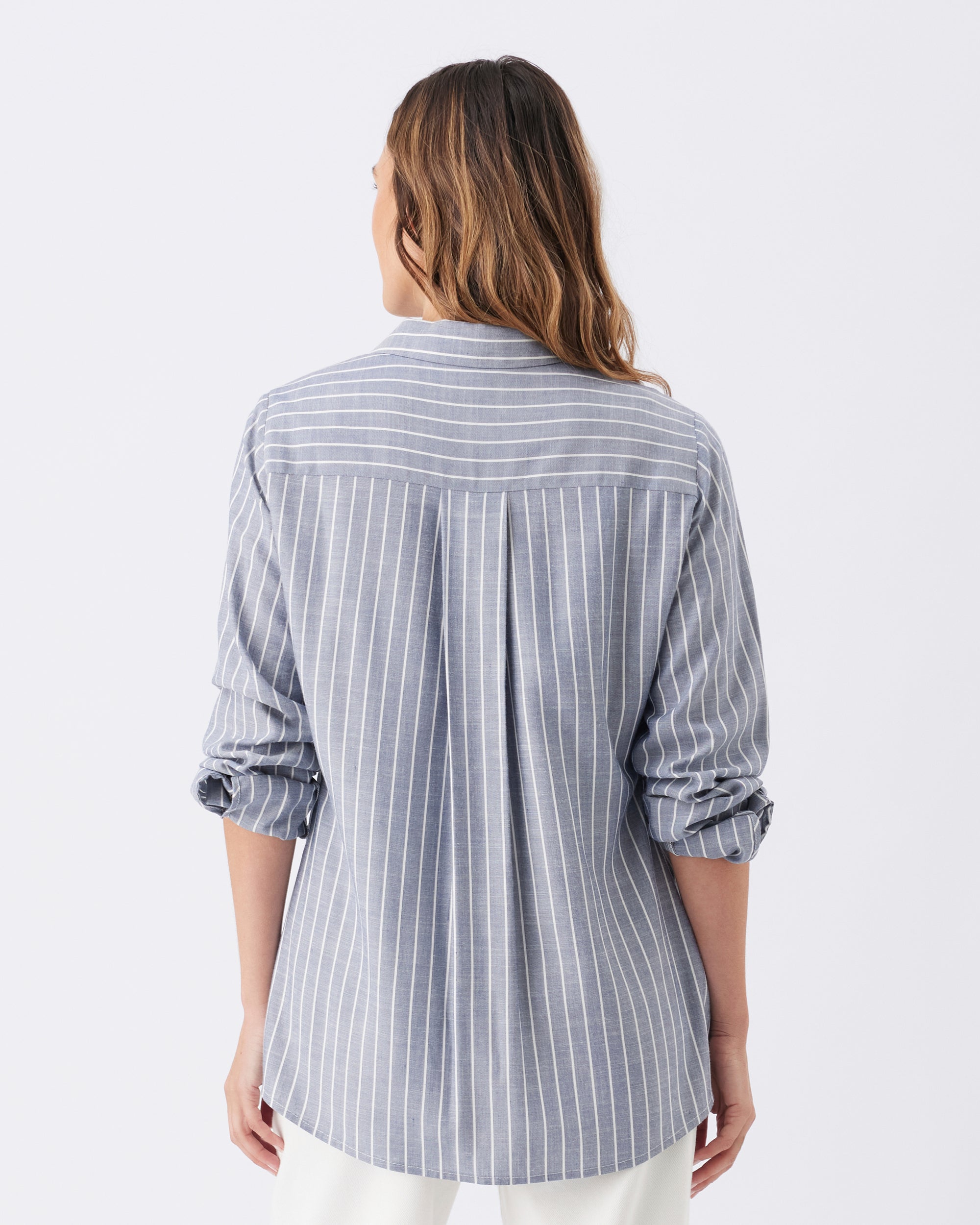 Back view of a woman wearing a striped shirt with the sleeves rolled up on a white background