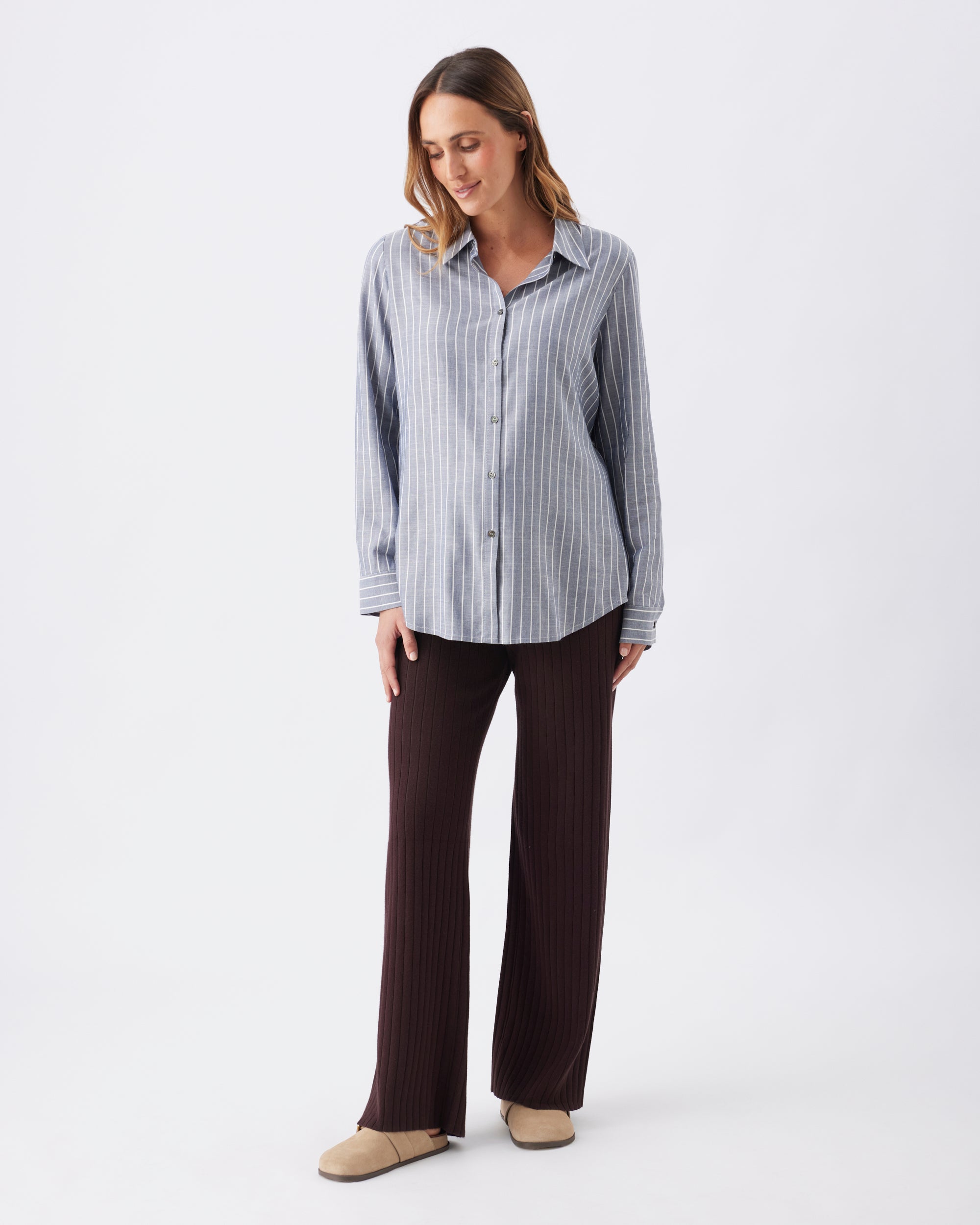 Woman wearing a light blue striped shirt and dark pants on a white background
