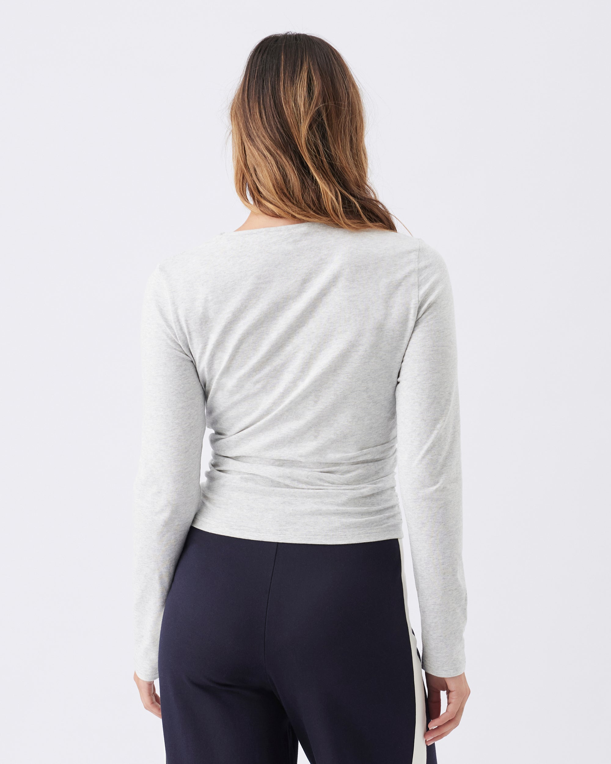 Back view of a woman wearing a light gray long-sleeve top and dark blue leggings on a white background